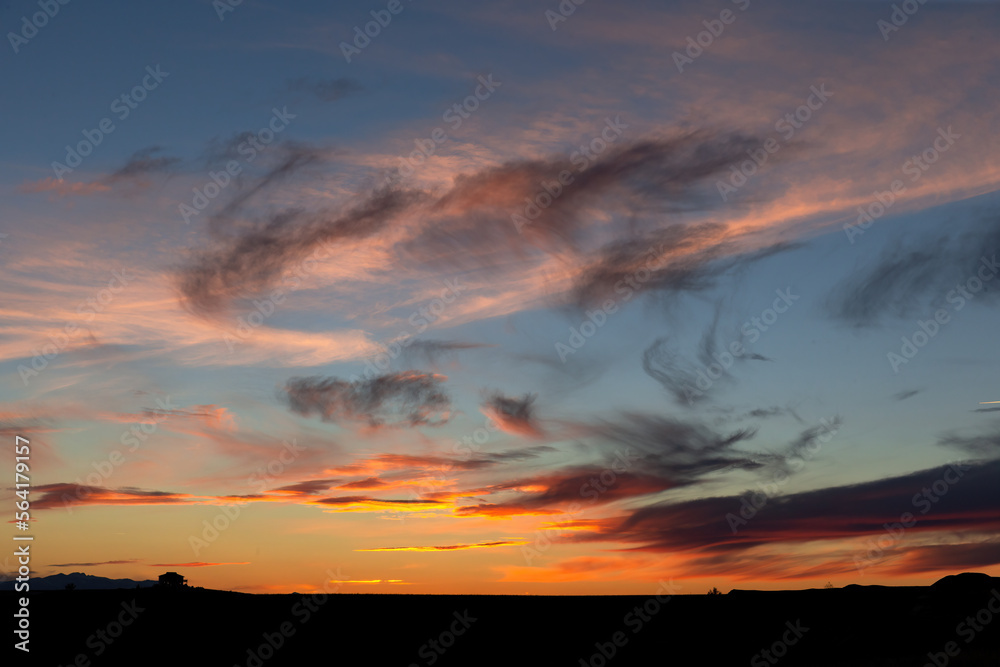 Obraz premium Large ranch house silhouette in the distance at the horizon dwarfed by sunrise or sunset in Montana for scale to show big sky country