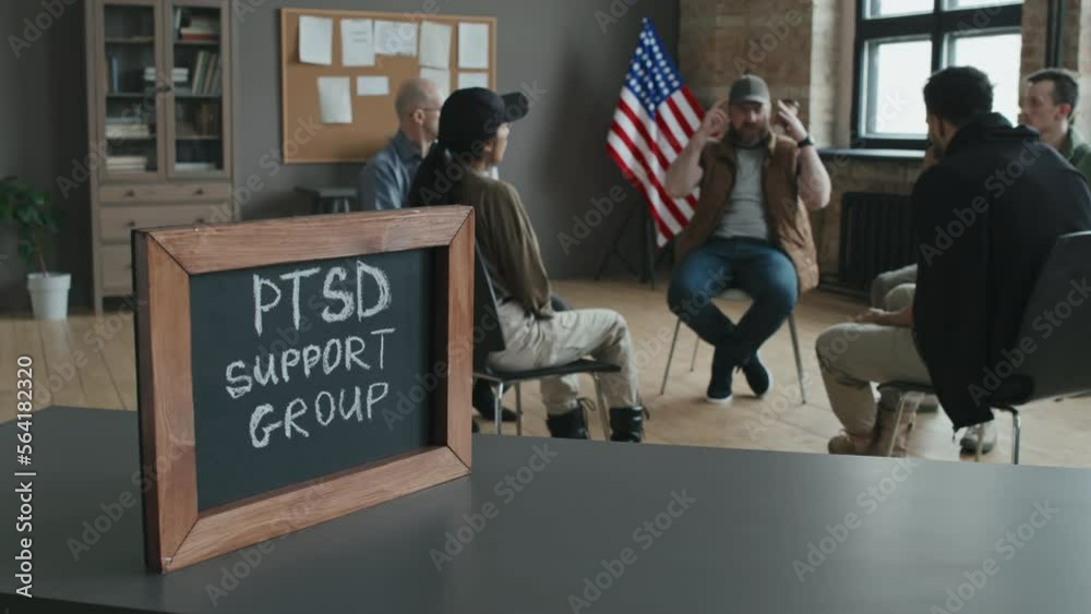 Selective focus shot of small blackboard with chalk inscription in wooden frame on table, PTSD support group discussing problems on background
