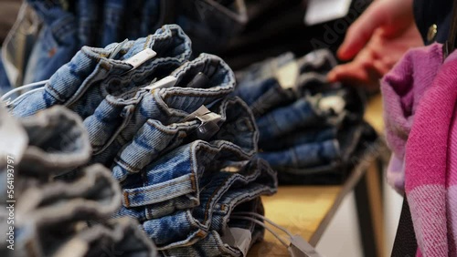 A man in the background is selecting jeans from a display in a retail store. The focus is on neatly stacked denim, showcasing the variety available for shoppers to choose.