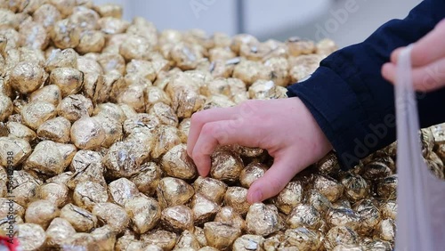 Hand reaches to select a piece of gold-wrapped candy from a large pile of chocolates. The action captures the appeal of choosing and enjoying sweets, emphasizing delight and choice.