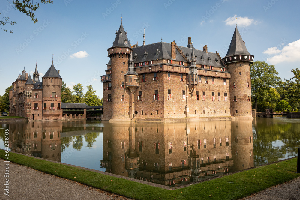 outside of Kasteel De Haar Dutch medieval castle reflection in moat on sunny summer day. Flowers match colour of Utrecht Netherlands where historic building with European architecture is located