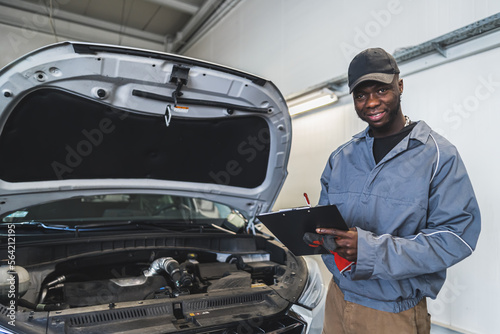 Skilled car technician inspects the engine at a repair facility and taking notes. High-quality photo
