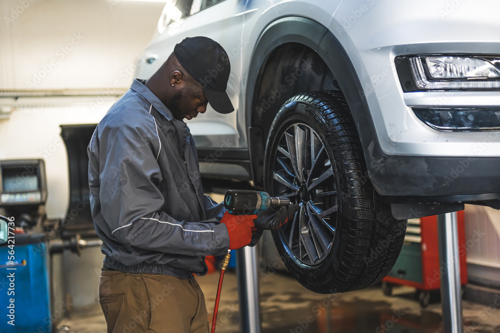 A mechanic working on a lifted-up car - Changing wheels using an electric wrench. High-quality photo