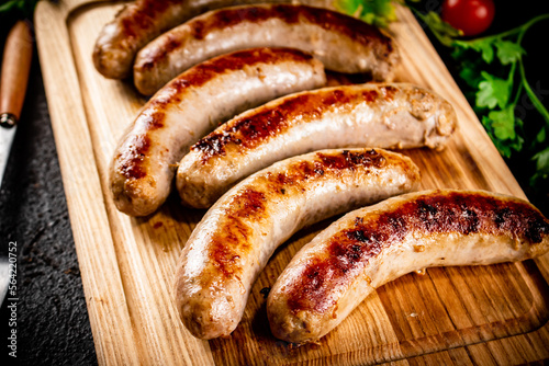 Grilled sausages on a wooden cutting board with parsley and tomatoes.