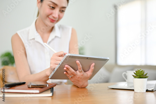 Beautiful millennial Asian woman using her digital tablet with stylus pen