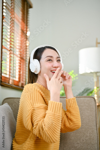 Joyful Asian woman enjoys listening to music through her headphones on sofa