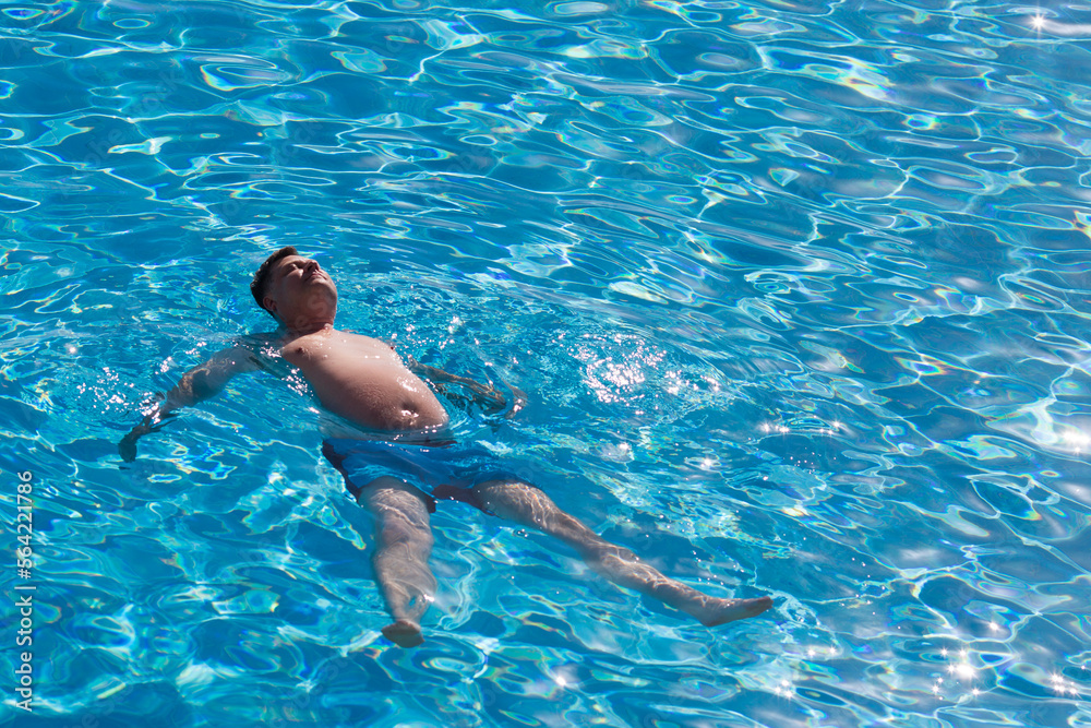 An adult large man swims on his back in a pool with clear blue water.