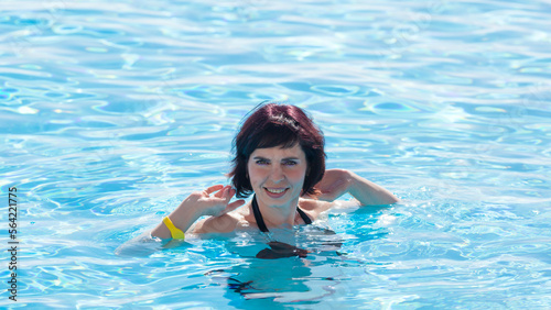 smiling adult woman is bathing in pool with clear blue water.