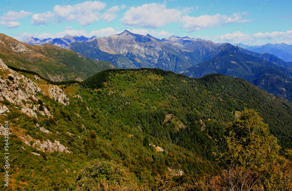 Panoramic view of the landscape with mountains and green hills in the foreground against a blue sky with clouds on Mount Cimetta, near Locarno in Switzerland
