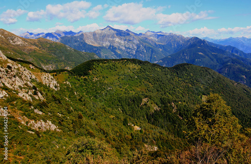 Panoramic view of the landscape with mountains and green hills in the foreground against a blue sky with clouds on Mount Cimetta, near Locarno in Switzerland