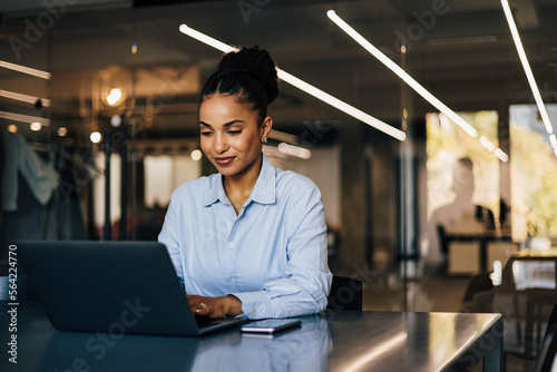An adult African businesswoman working at the office using a laptop, elegantly dressed.