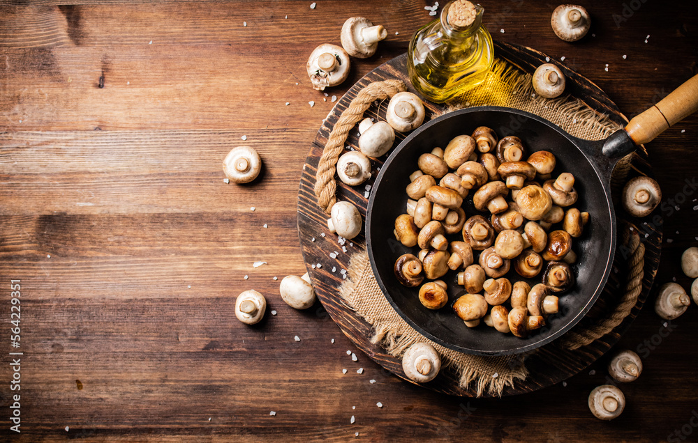 Frying pan with fried mushrooms on a wooden tray. Frying pan with fried mushrooms on a wooden tray.