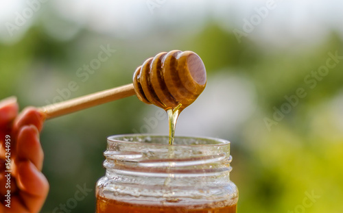 Honey flows from a wooden stick into a jar.