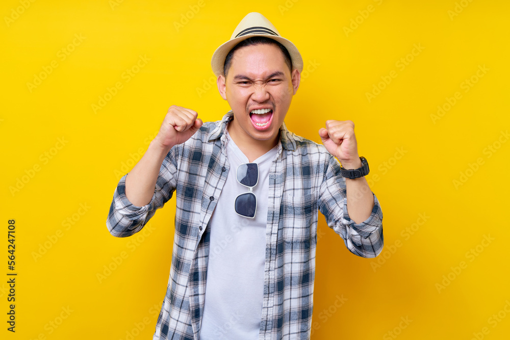 excited fun Young handsome ethnic Asian man 20s wearing casual clothes hat making winner gesture celebrating clenching fists saying yes isolated on yellow background. People lifestyle concept excited fun Young handsome ethnic Asian man 20s wearing casual clothes hat making winner gesture celebrating clenching fists saying yes isolated on yellow background. People lifestyle concept
