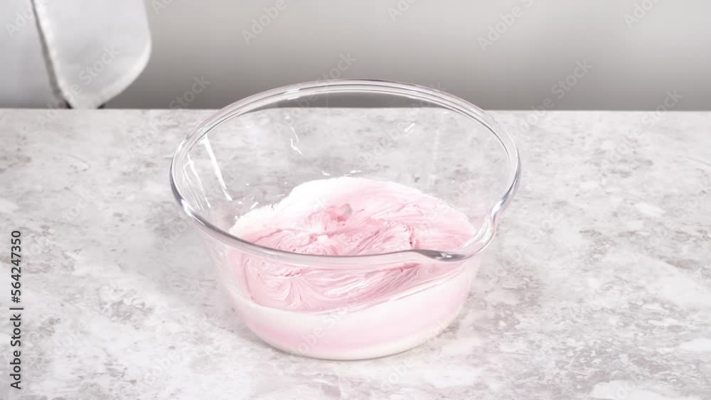 Scooping pink vanilla buttercream frosting into a piping bag. Scooping pink vanilla buttercream frosting into a piping bag.