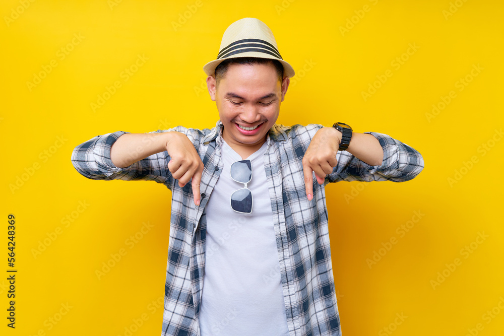 Smiling Young handsome ethnic Asian man 20s wearing casual clothes hat standing pointing index fingers down on mock up copy space isolated on yellow background. People lifestyle concept Smiling Young handsome ethnic Asian man 20s wearing casual clothes hat standing pointing index fingers down on mock up copy space isolated on yellow background. People lifestyle concept