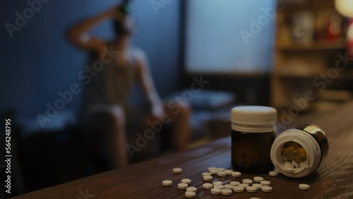 Selective focus close-up of two jars with antidepressant pills or hypnotic drugs on table, unrecognizable man taking them on background