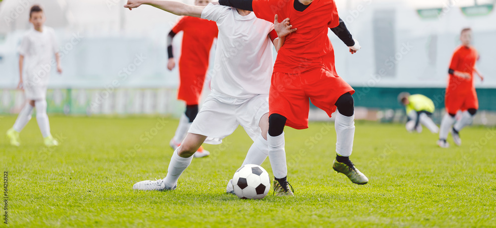 Obraz premium Soccer players duel. Soccer youth tournament game. Footballers compete for a soccer ball on a grass pitch during a junior level match