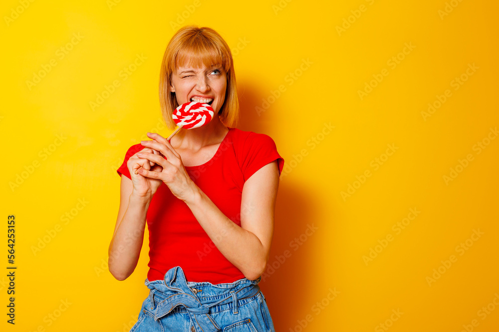 Woman biting candy on yellow background Woman biting candy on yellow background