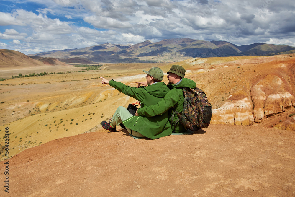 couple of tourists sit with their backs to camera against backdrop of landscape on summer day. Sights of Russia, Siberia and Altai Republic, mars. Tourism and travel. Kosh-agach, Chagan-Uzun