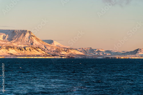 imagen de unas montañas iluminadas con las ultimas luces del día con el mar a sus pies, el cielo azul y algunas nubes photo