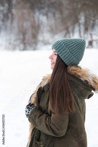 A young girl, brunette, in sweater, a hat and an green jacket, against the backdrop of the winter landscape. Snow and frost, the concept of Christmas.