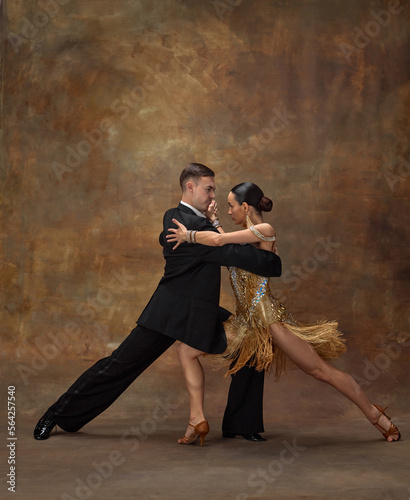 Attraction, passion, emotions. Man and woman, professional dancers in stylish, beautiful stage costumes performing ballroom dance over dark vintage background. Concept of hobby, lifestyle, action