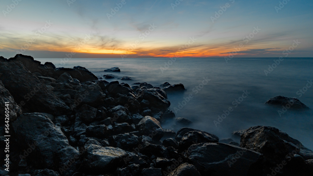 Wide angle long exposure shot of sunset at sea. Coastal rocks in the foreground. Black sea shore.