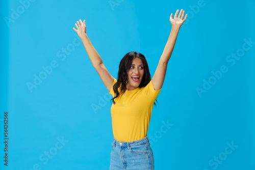 Woman in yellow t-shirt on blue background posing gestures emotions and signals with smile, hands up happiness copy space