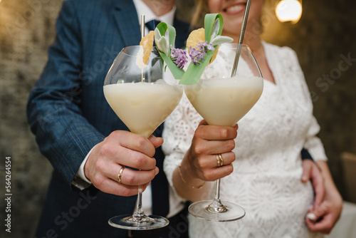 Fototapeta Naklejka Na Ścianę i Meble -  Couple drinking cocktail Pina Colada with a slice of pineapple. The bride and groom are holding cocktails. Honeymoon concept after the wedding. Close up.