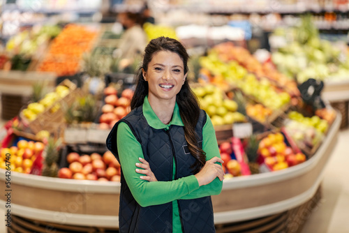 A happy sales manager is standing with arms crossed in supermarket and smiling at the camera. photo