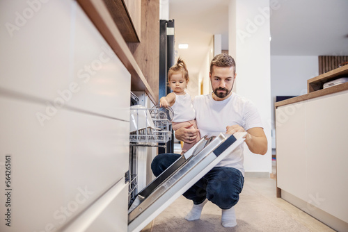 A father and baby girl are putting dishes into a dishwasher together.