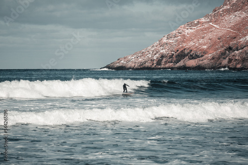 Arctic surfer in Unstad beach, Lofoten, Norway during cold winter time with big waves 