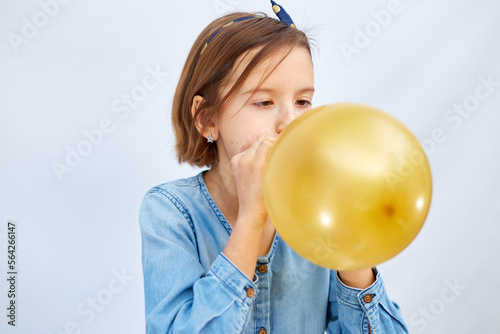Fotografia Pretty little girl in casual denim dress blowing, inflate yellow balloon on whit