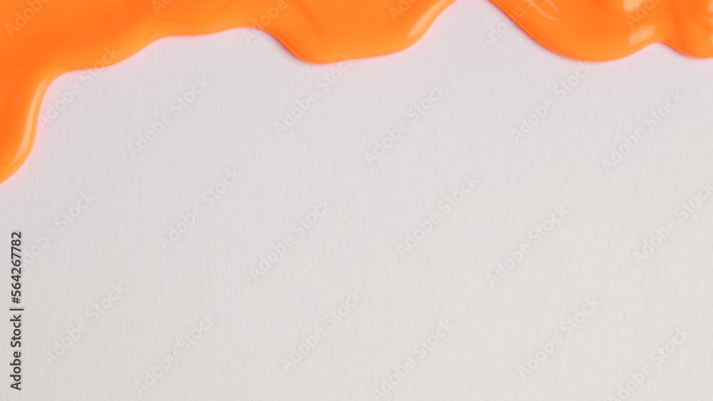 Liquid drops of orange paint color flowing on the white surface. Macro shot of orange paint dripping on the white wall with copy space. Production Close-up. Slow Motion, Abstract art.
