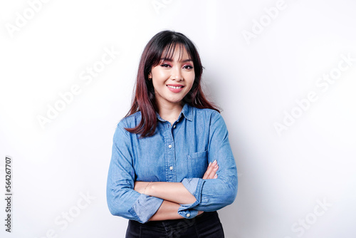 Portrait of a confident smiling Asian woman wearing blue shirt standing with arms folded and looking at the camera isolated over white background