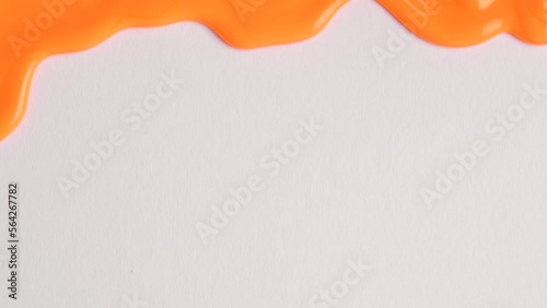 Liquid drops of orange paint color flowing on the white surface. Macro shot of orange paint dripping on the white wall with copy space. Production Close-up. Slow Motion, Abstract art.