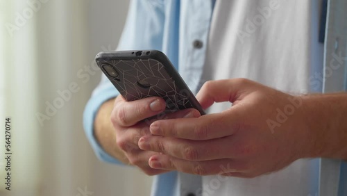Close up young man holding smartphone in hands, scrolling news feed, web surfing information, shopping in internet store or communicating distantly with friends online, tech addiction concept.
