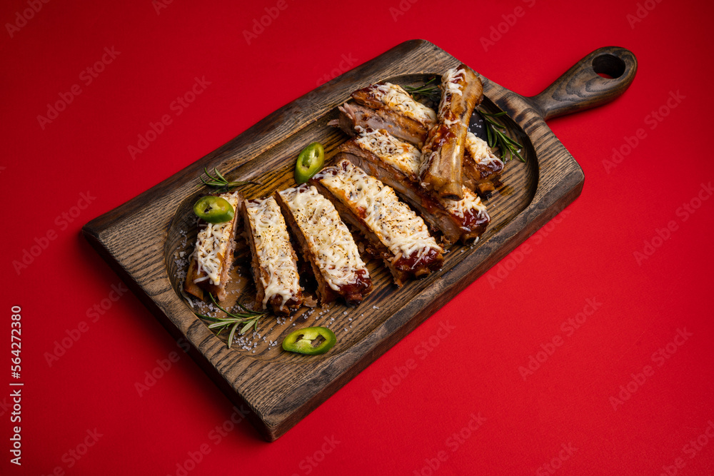 grilled pork ribs in tomato sauce with cheese on a board on a red background
