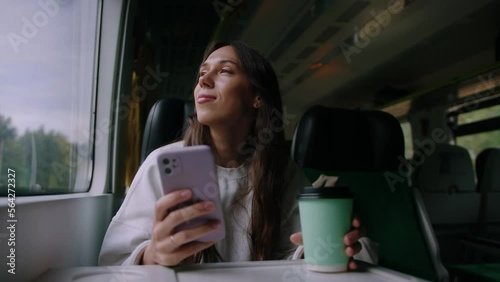 A young woman is traveling alone by train. The brunette drinks coffee and enjoys the trip