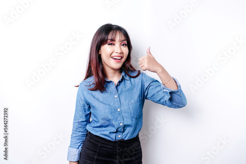 Excited Asian woman wearing blue shirt gives thumbs up hand gesture of approval, isolated by white background © Reezky