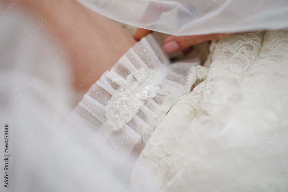 Bride dresses garter on the leg. Picture of beautiful female legs in wedding dress. Bride putting a wedding garter on her leg. Top view. Bride dresses garter on the leg. Picture of beautiful female legs in wedding dress. Bride putting a wedding garter on her leg. Top view.