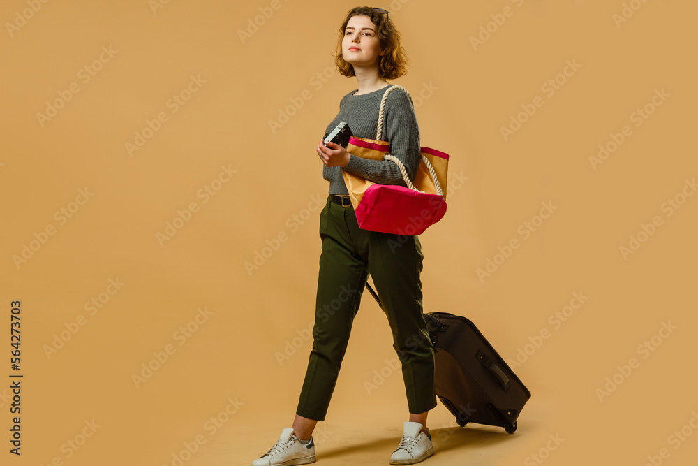 concept of travel. happy woman girl with suitcase and passport on yellow colored background.