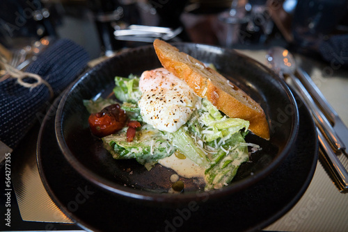 Caesar Salat mit Baguette und einem blanchiertem Ei auf schwarzem Steinteller