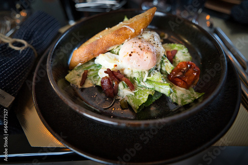 Caesar Salat mit Baguette und einem blanchiertem Ei auf schwarzem Steinteller