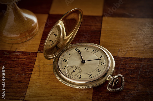 An antique gold pocket watch lies on a chess board