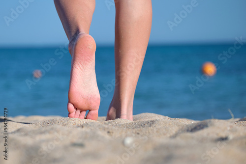 Close up of female feet walking barefoot on white grainy sand of golden beach on blue ocean water background photo