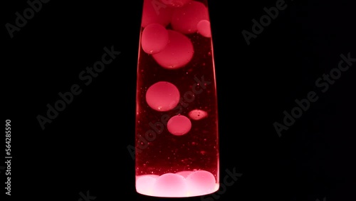 Close macro shot of red lava lamp. Moving doubles of hot red wax inside a lava lamp in front of black background.
