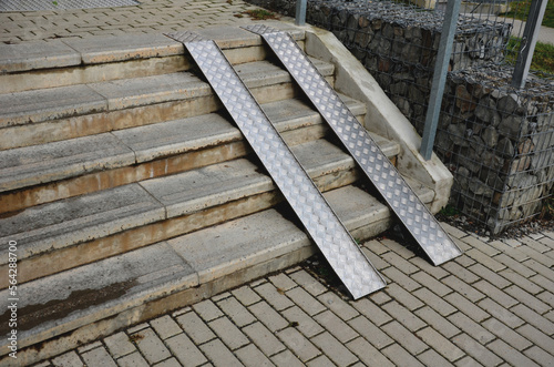 ramp combined with a gray concrete staircase and a handrail specially adapted for wheelchairs. security tasteful solution for entering a city park. sheet metal rails, pram, mother, wheels