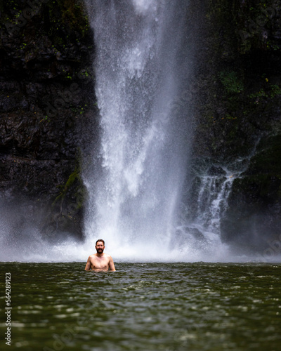 A man stands in the water beneath the mighty nandroya falls in wooroonooran national park in queensland, australia; swimming in a waterfall in the atherton tablelands
